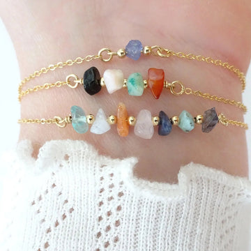 Two gold anklets with colorful beads on a person's ankle against a white background.